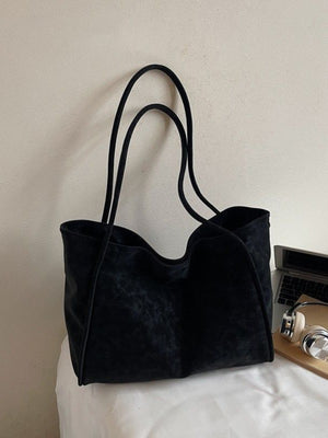 Large black suede shoulder bag with thin straps and a subtle charm detail.