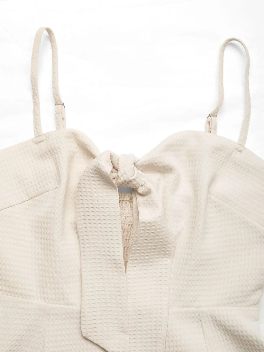 Beige textured romper with tie-front detail and smocked bodice.
