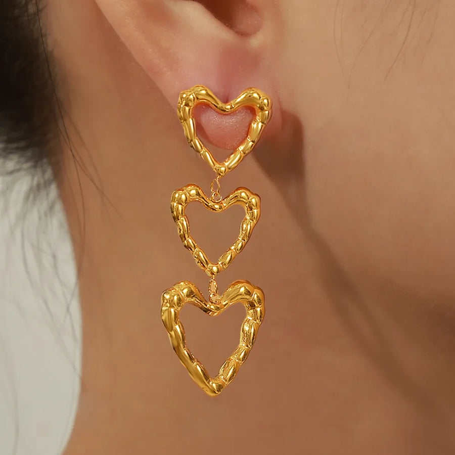Gold triple heart drop earrings with textured detail.