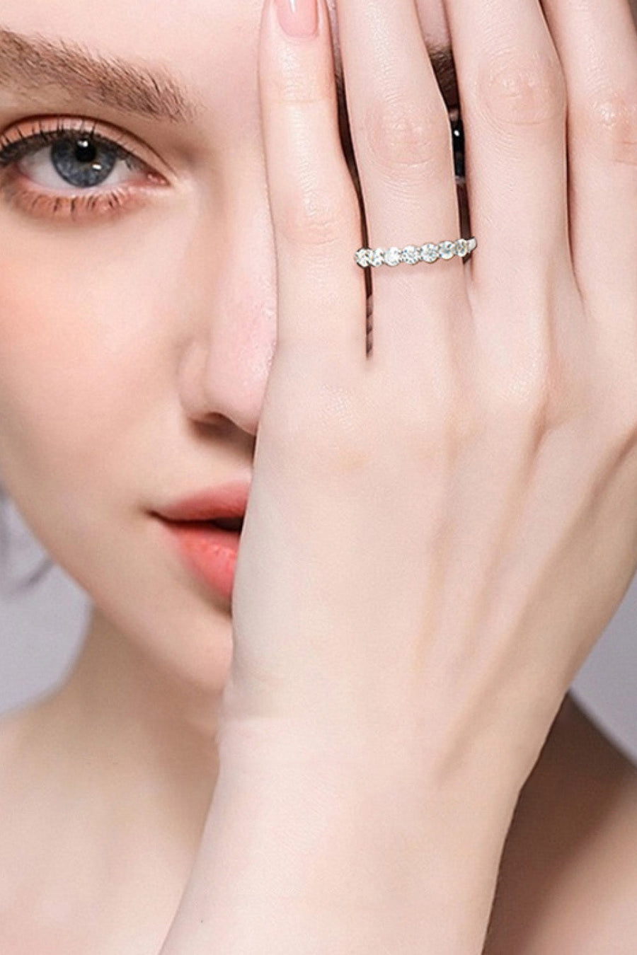 Silver band ring with seven clear stones on a woman's finger.