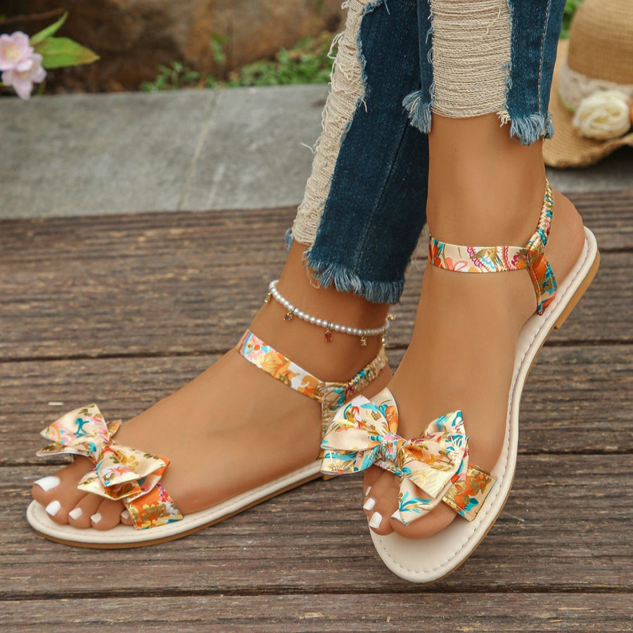 Floral bowknot flat sandals in beige with colorful print and ankle strap.