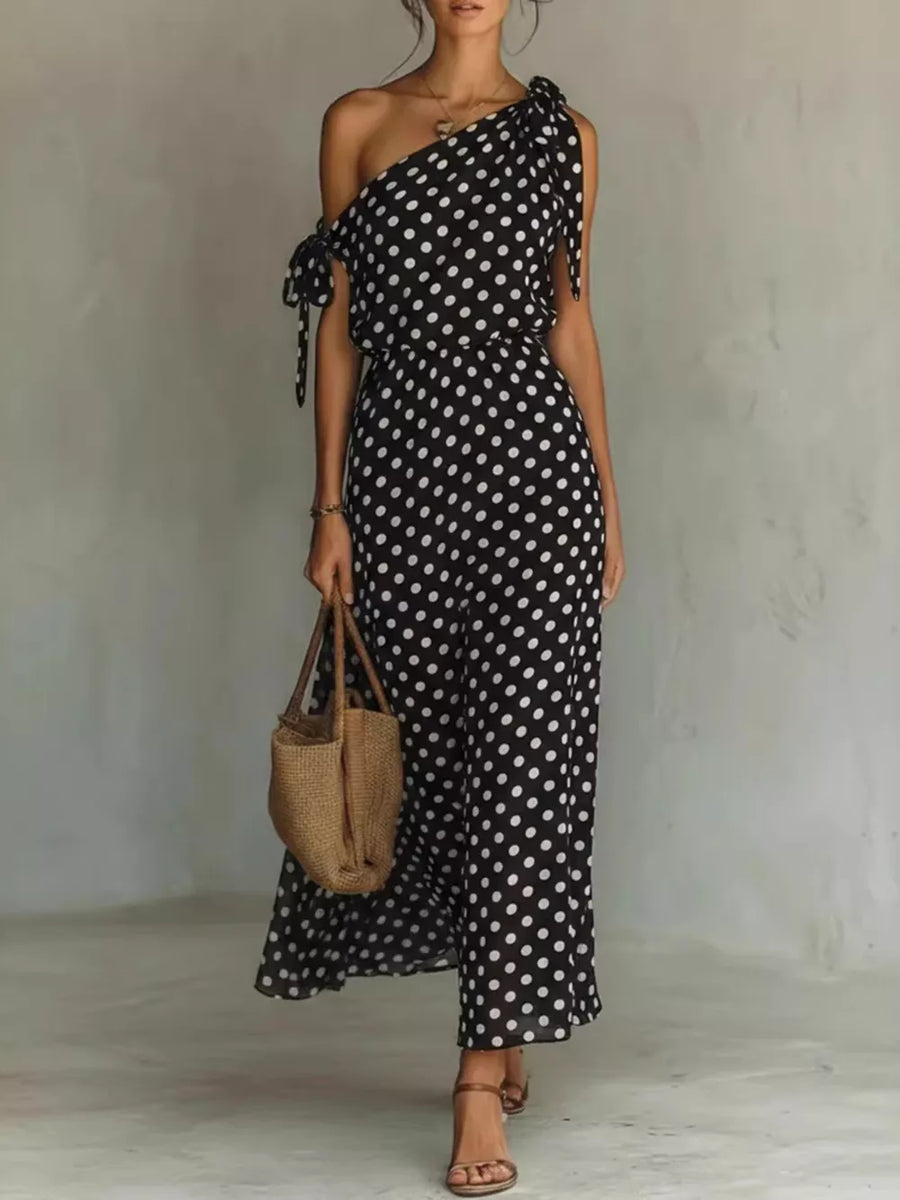 Black polka dot one-shoulder maxi dress with tie details and a flowing skirt.