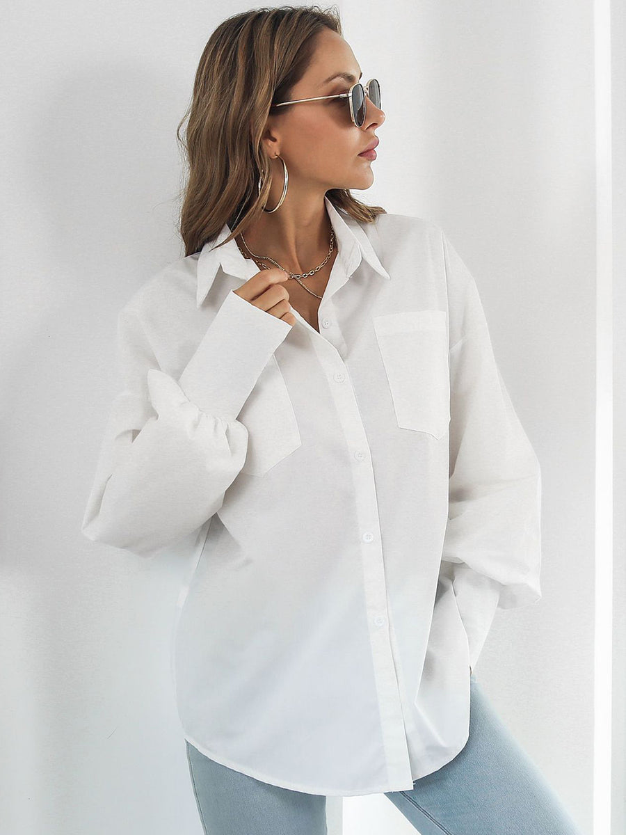 White oversized poplin blouse with blouson sleeves and button front, styled with jeans.