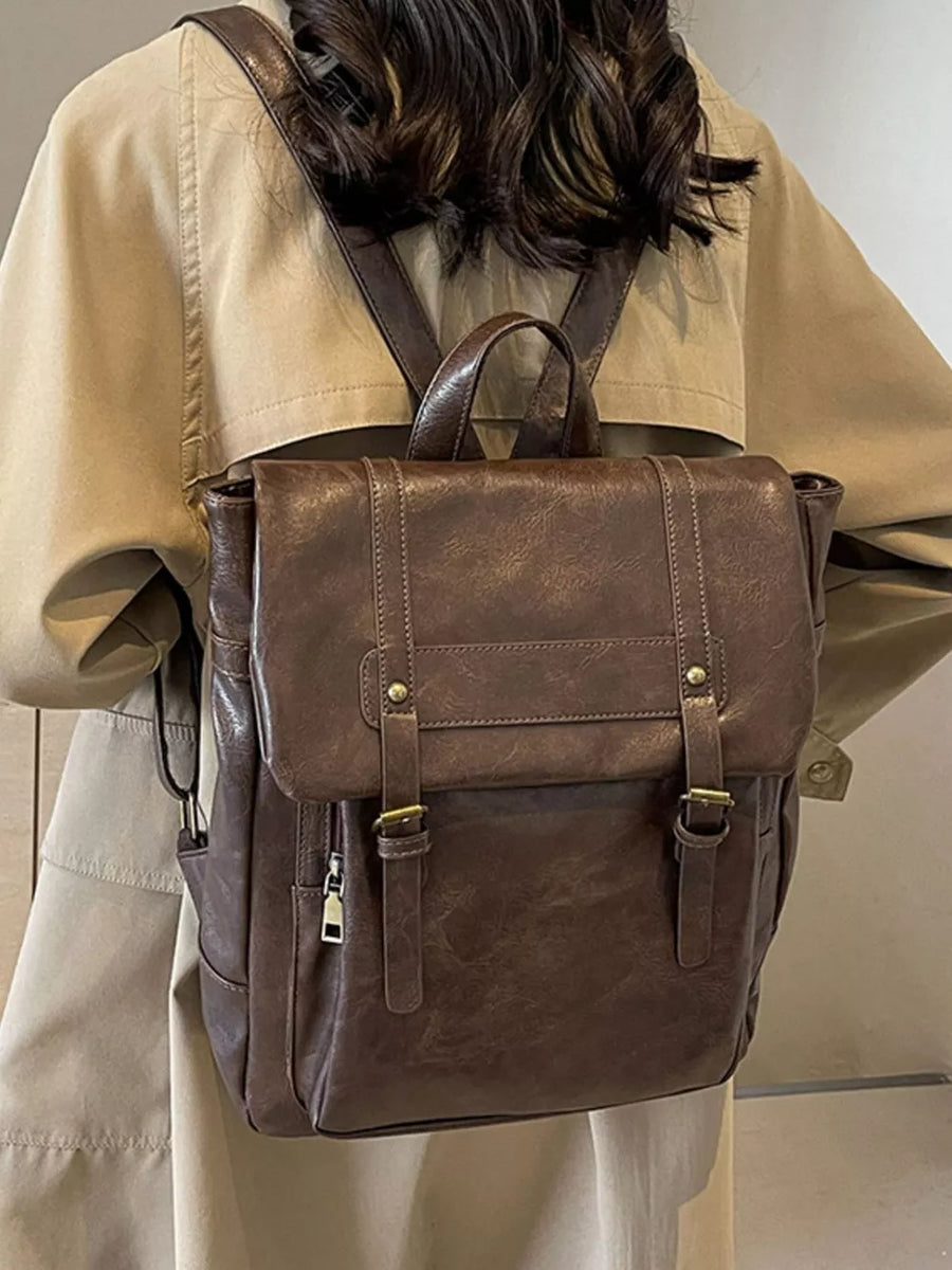 Brown pu leather flap backpack with brass hardware and adjustable straps.