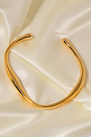Gold 18K gold-plated open-ended bangle with a sculpted, fluid design on satin.