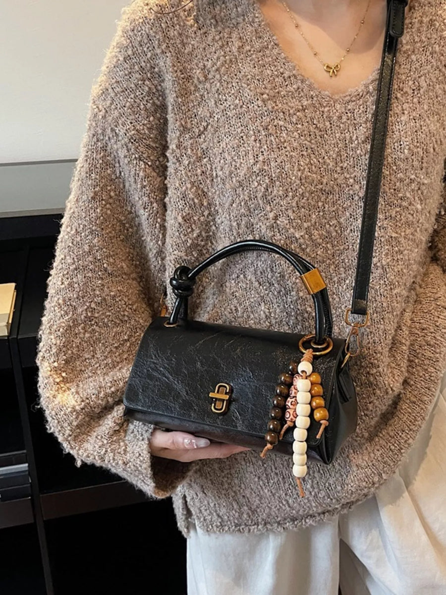 Black leather crossbody bag with beaded charm and gold clasp detail