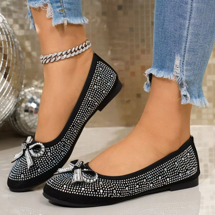 Black rhinestone-embellished bow flats with a silver anklet.
