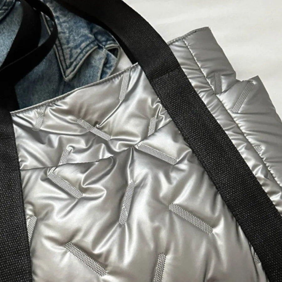 Padded silver nylon tote bag with black straps and exterior pockets, featuring a quilted pattern.