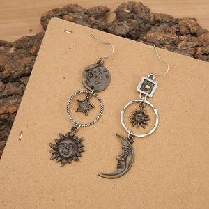 Cosmic asymmetry drop earrings in copper feature sun, moon, and star charms with unique celestial designs.