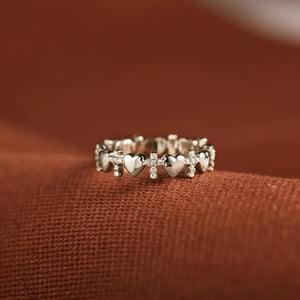 Sterling silver band ring with alternating heart and cross charms, accented with small stones.