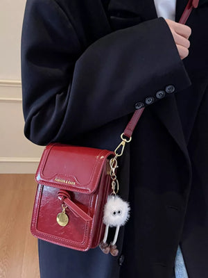 Deep Red mini crossbody bag in shiny pu leather with a fuzzy charm accessory.