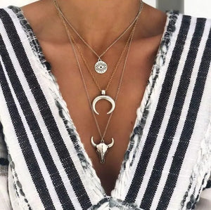Silver layered pendant necklace with evil eye, crescent moon, and bull skull charms.