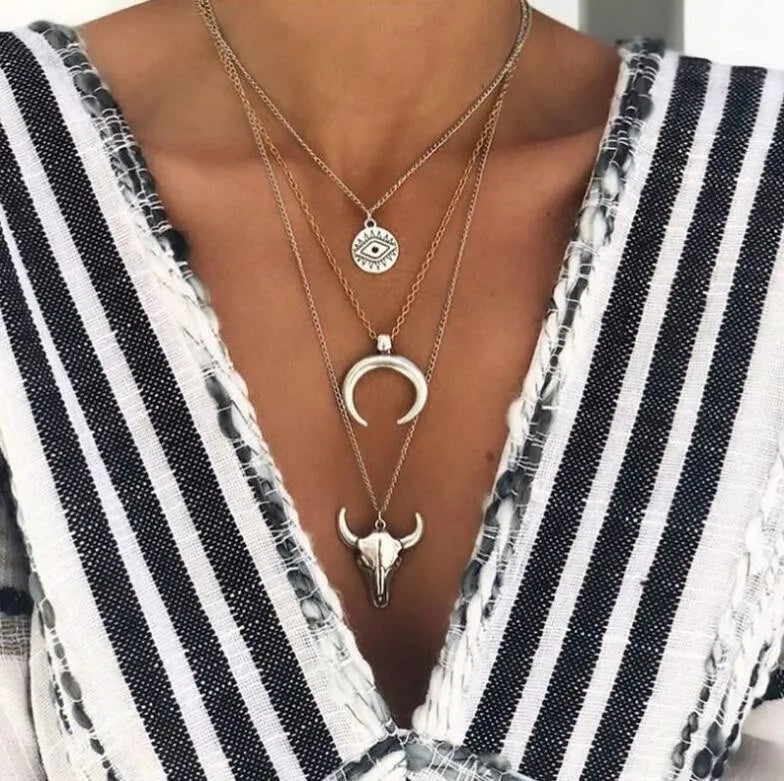 Silver layered pendant necklace with evil eye, crescent moon, and bull skull charms.