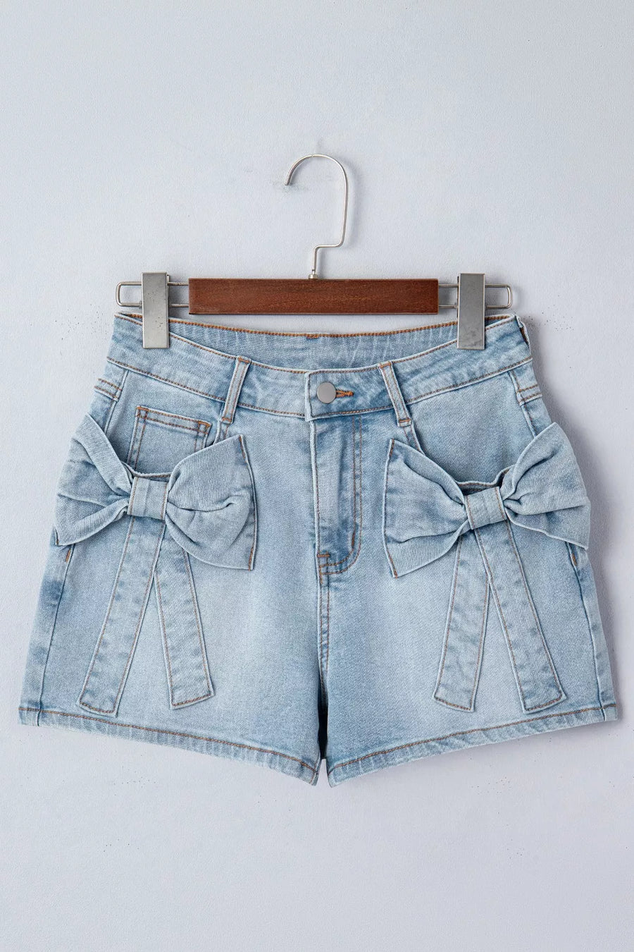 Light wash denim shorts with bow embellishments on pockets and button fly.
