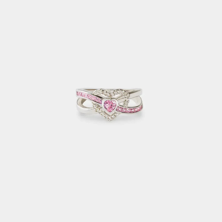 Silver ring with intertwined infinity band and a pink heart-shaped zirconia center surrounded by small clear stones.