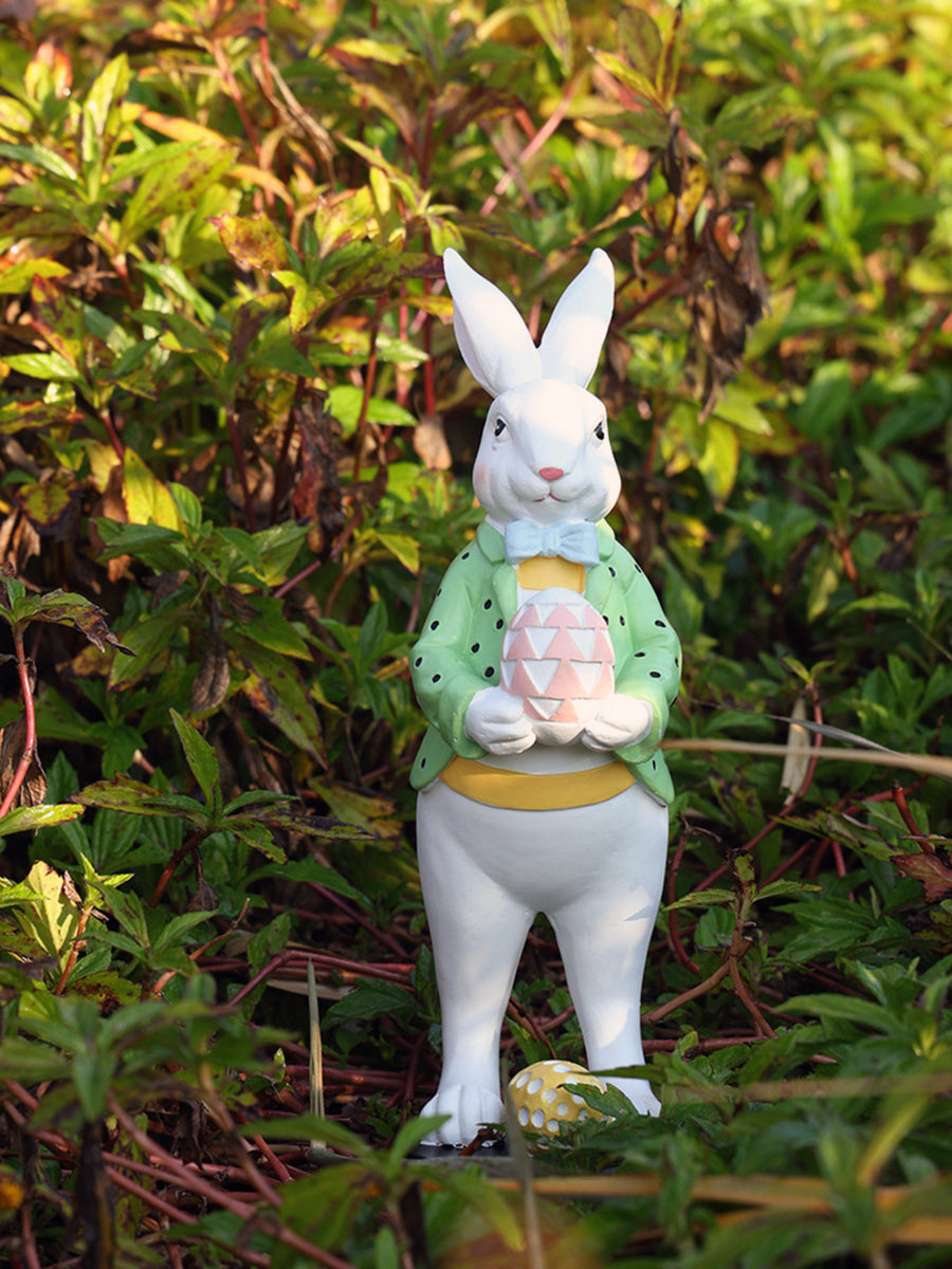 Easter bunny figurine in a green polka dot jacket and blue bow tie holding a pink patterned egg.