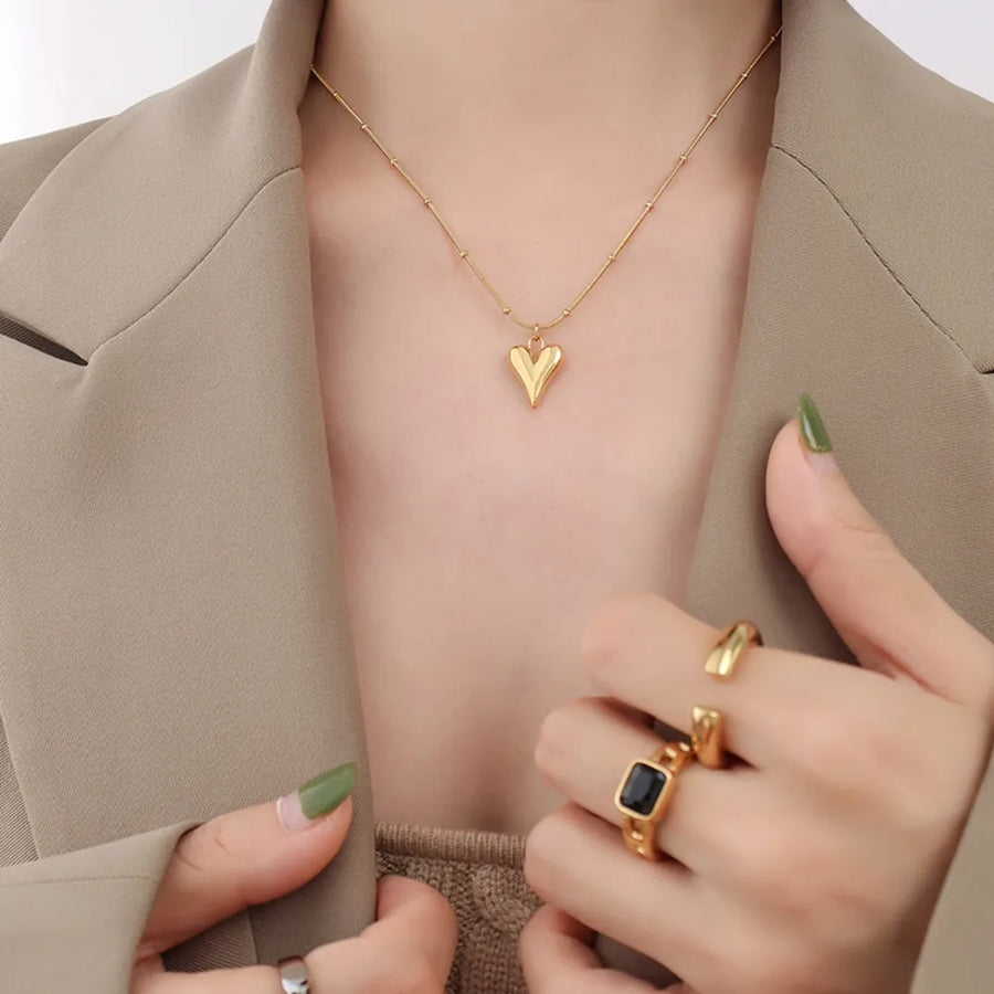 Gold heart pendant necklace with beaded chain, worn with rings.