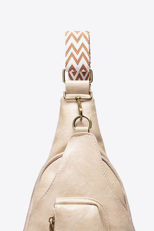 Beige textured sling bag with woven chevron strap and gold hardware detail.