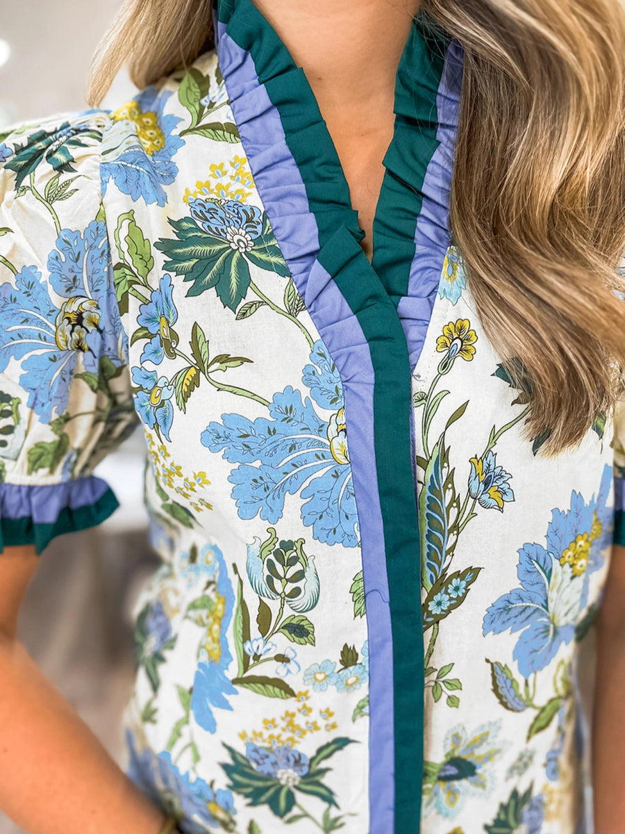 Floral frilled blouse with blue, green, and yellow flowers, featuring striped trim and ruffled cuffs.