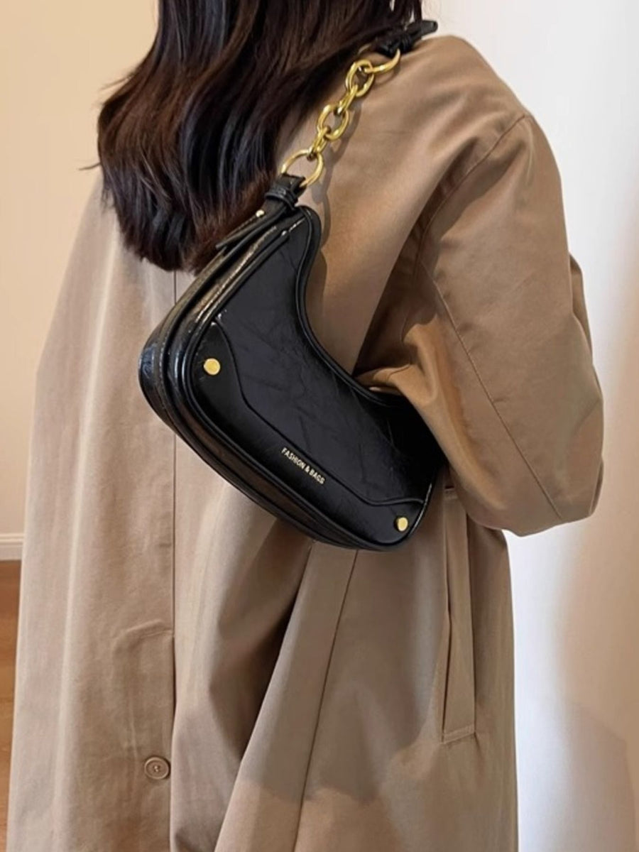 Black crescent shoulder bag with chunky gold chain and embossed text.