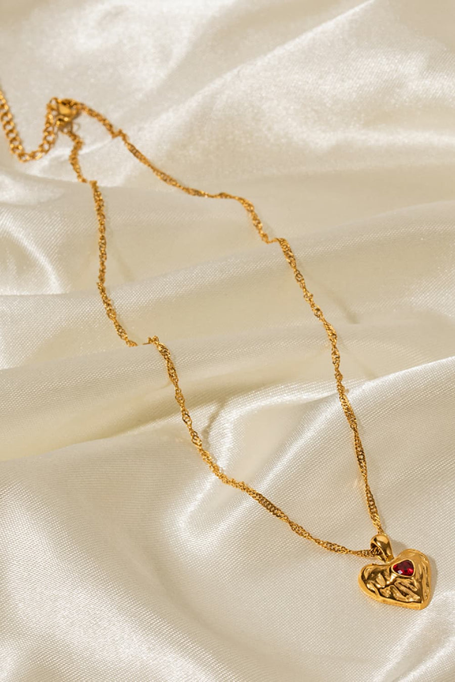Gold textured heart pendant necklace with red stone on a delicate chain.