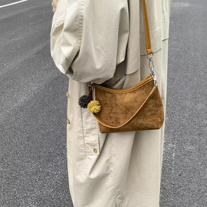 Brown suede crossbody bag with pom-pom charms and adjustable strap.