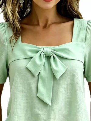 Light green puff sleeve shirt with a large bow tie detail on a square neckline.