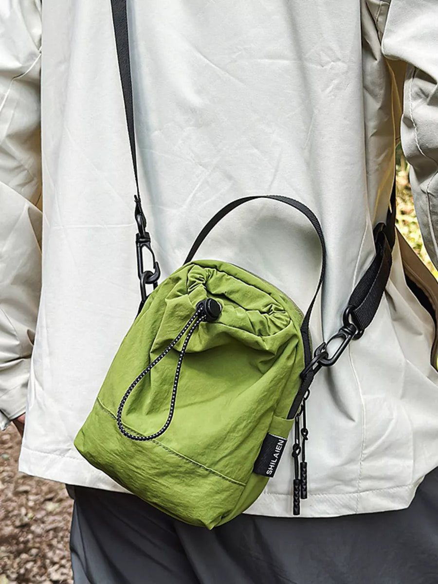 Green nylon drawstring shoulder bag with black strap and zipper pulls.