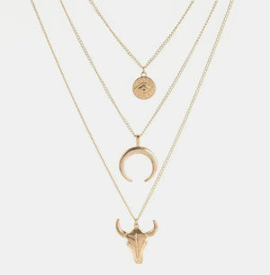 Gold layered pendant necklace with evil eye, crescent moon, and bull skull charms.