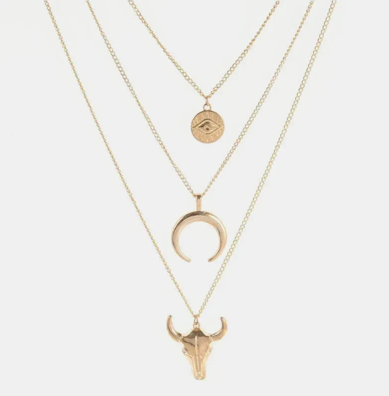 Gold layered pendant necklace with evil eye, crescent moon, and bull skull charms.