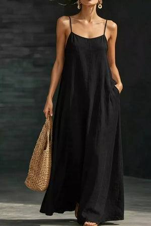 Black A-line maxi dress with spaghetti straps and pockets, worn with a straw bag.