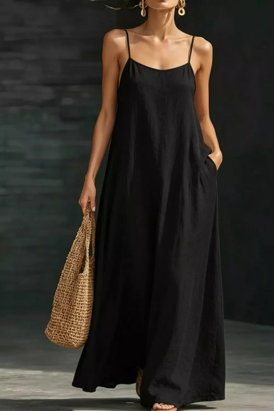 Black A-line maxi dress with spaghetti straps and pockets, worn with a straw bag.