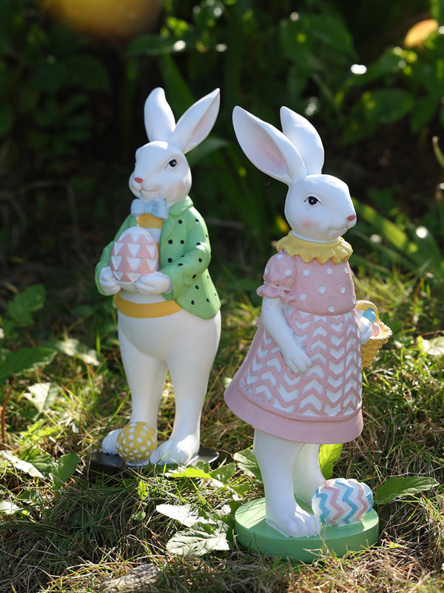 Easter bunny figurines in blush pink and gum leaf green, holding decorative eggs.