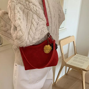 Red suede crossbody bag with yellow pom-pom charm and adjustable strap