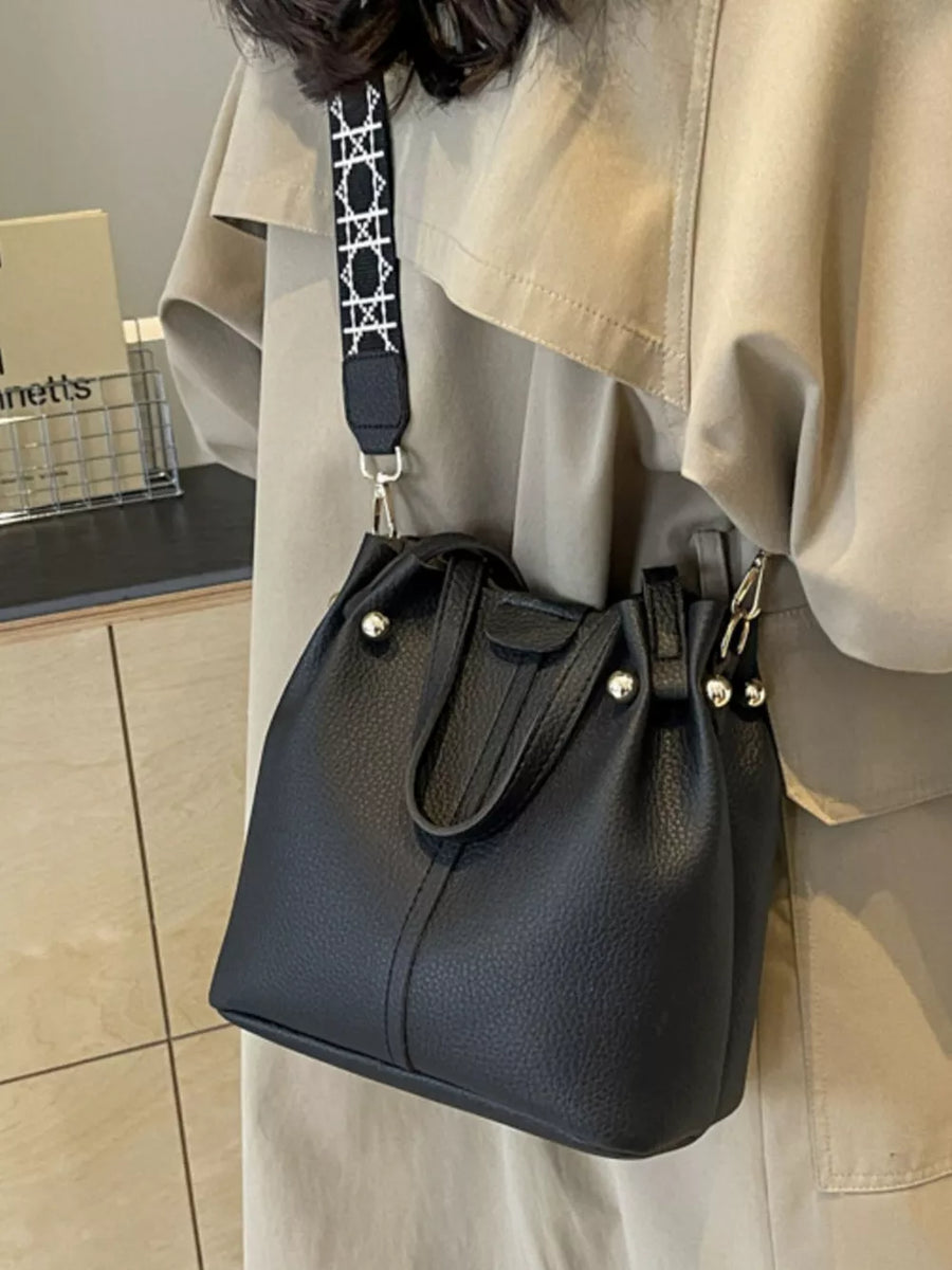Black textured crossbody bag with unique patterned strap and silver hardware.