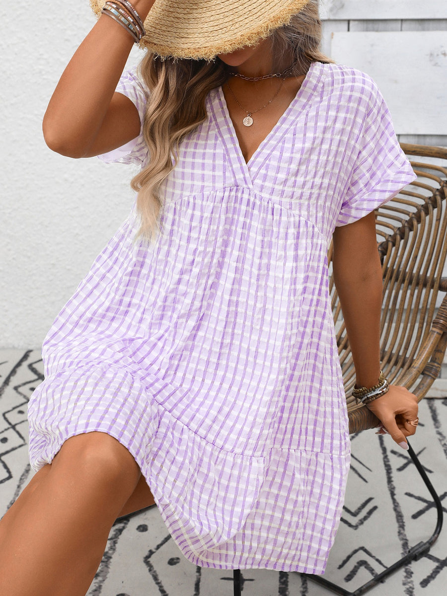 Plaid v-neck mini dress in purple and white gingham with short sleeves and tiered hem.