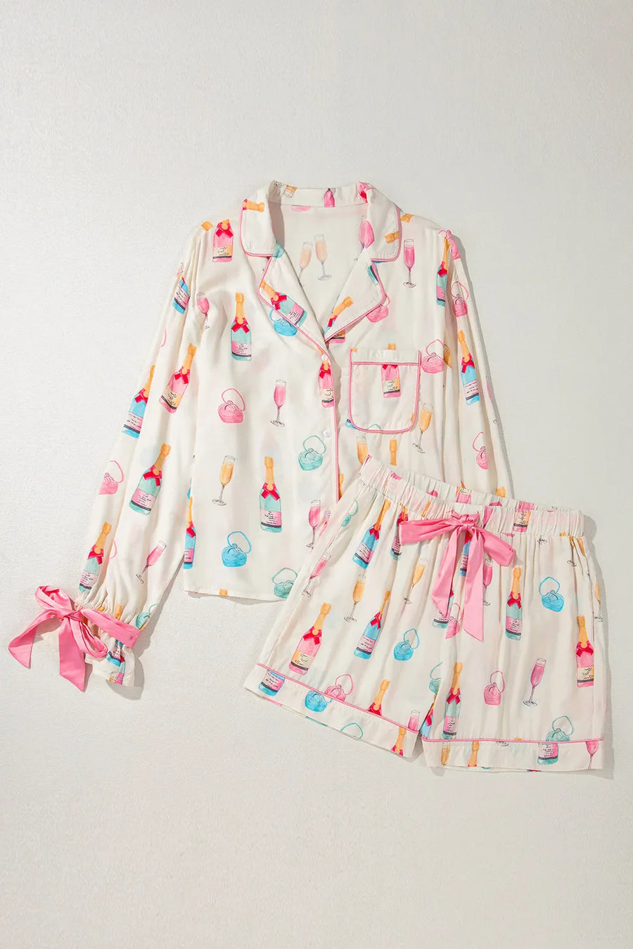White silk pajama set with champagne print, pink piping, and bow details on sleeves and shorts.