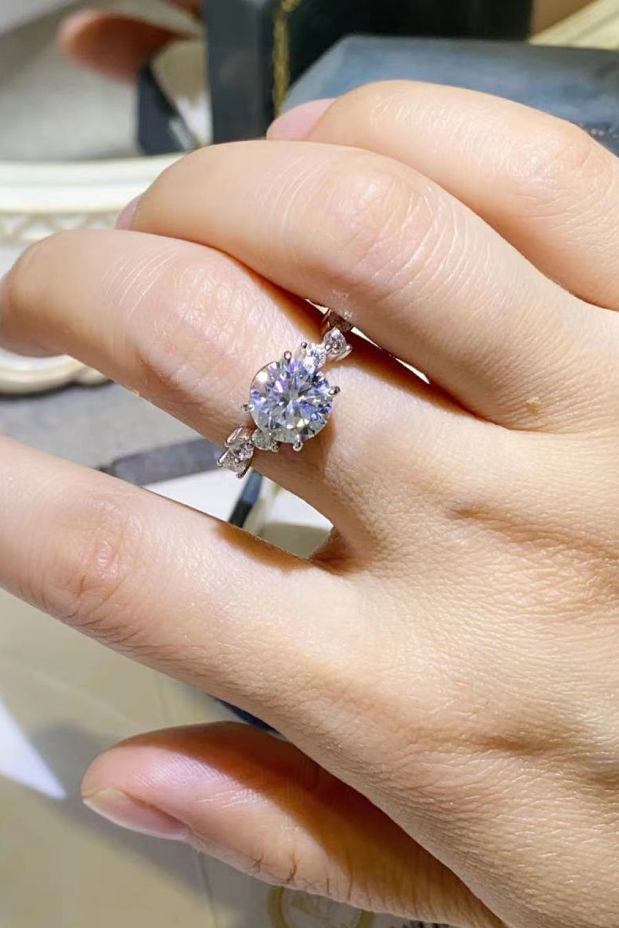 Silver moissanite halo ring with a central round-cut stone and delicate side accents.