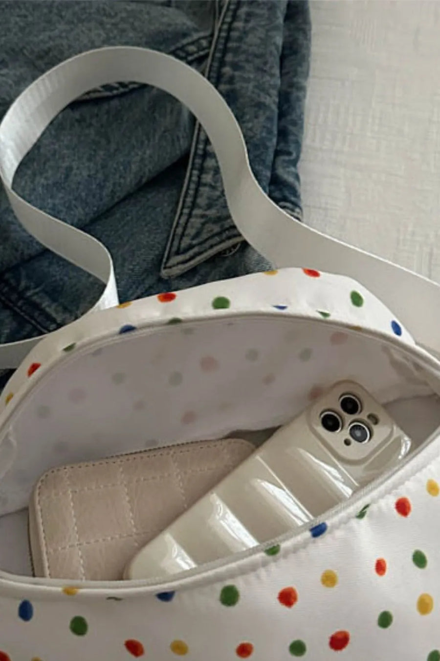 White polka dot belt bag with colorful dots, showing interior wallet and phone.