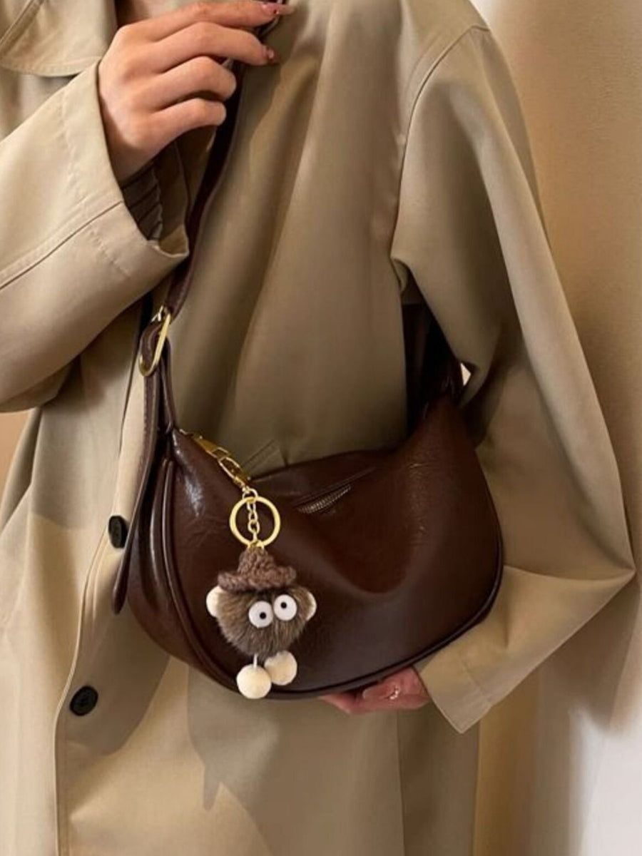 Brown crescent shoulder bag with plush charm and adjustable strap