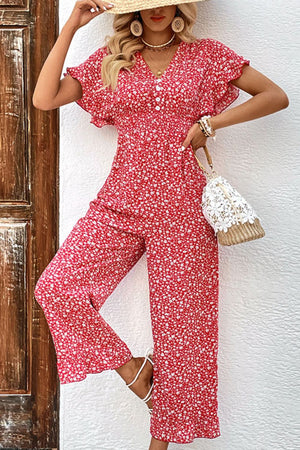 Smocked bodice floral jumpsuit with flutter sleeves and decorative buttons.