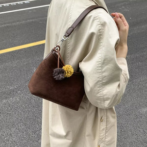 Brown suede crossbody bag with pom-pom charms and adjustable strap.