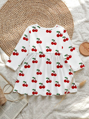White baby dress with allover red cherry print, long sleeves, and gathered waist.
