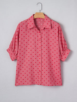 Pink button-down shirt with red heart pattern, classic collar, and cuffed sleeves.