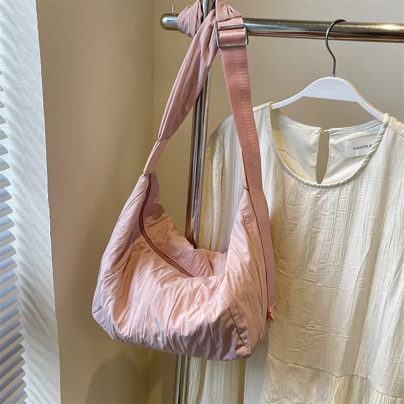 Pink quilted crescent shoulder bag with adjustable strap and zipper detail.