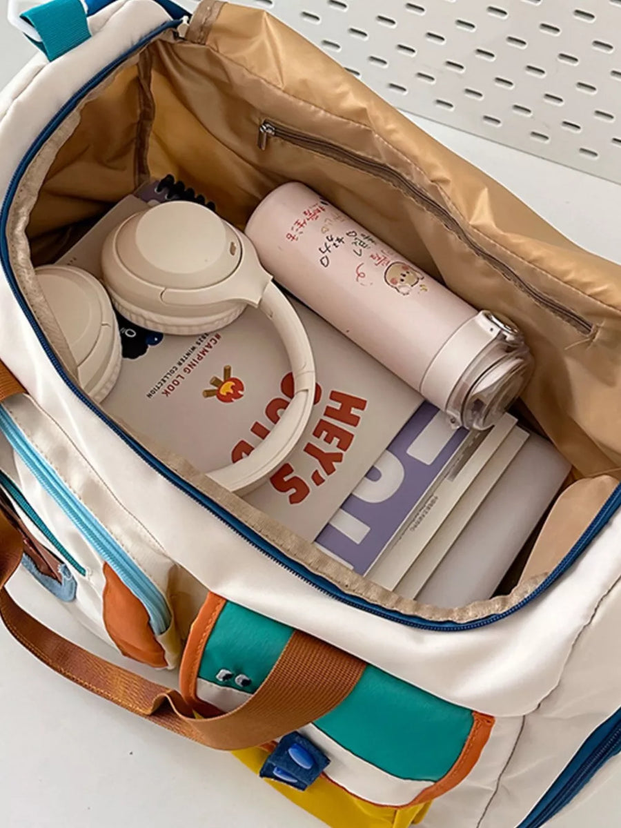 Vibrant multi-pocket nylon travel bag with color block details, shown packed with headphones and a water bottle.