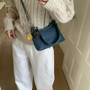 Blue suede crossbody bag with pompom charms and adjustable strap