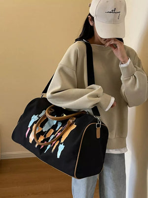 Black canvas duffle bag with colorful abstract star design and leather handles.