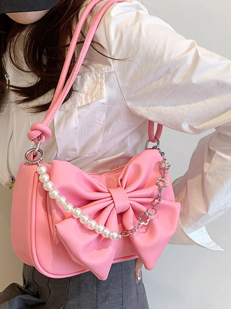 Pink shoulder bag with large bowknot detail and pearl chain strap.