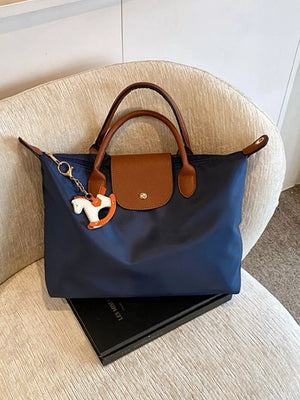Navy nylon tote bag with brown leather accents and a rocking horse charm.